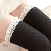 Black long socks with cable-like knit texture and contrasting pale lace cuffs, close-up