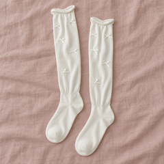 AI overhead pair illustration of white long ribbon-bow socks arranged vertically on muted rose linen