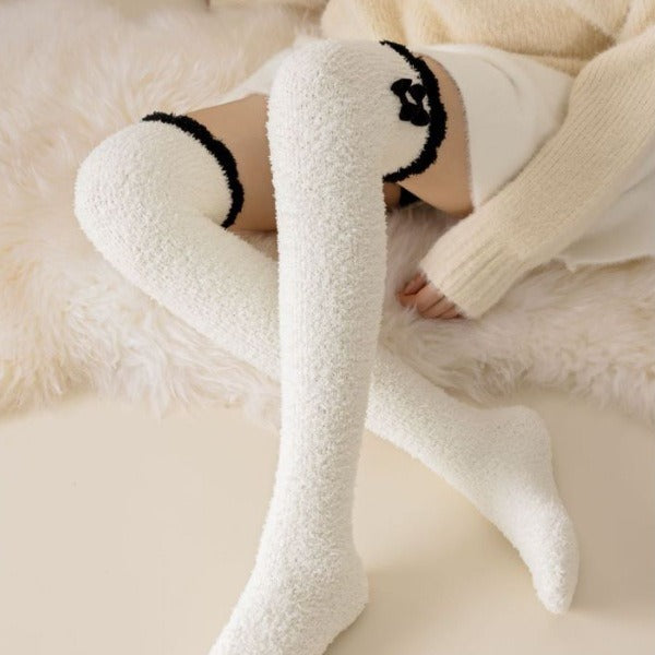 White fuzzy long socks with black cuff trim and stacked black bow detail, shown worn in a lounge outfit