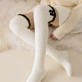 White fuzzy long socks with black cuff trim and stacked black bow detail, shown worn in a lounge outfit