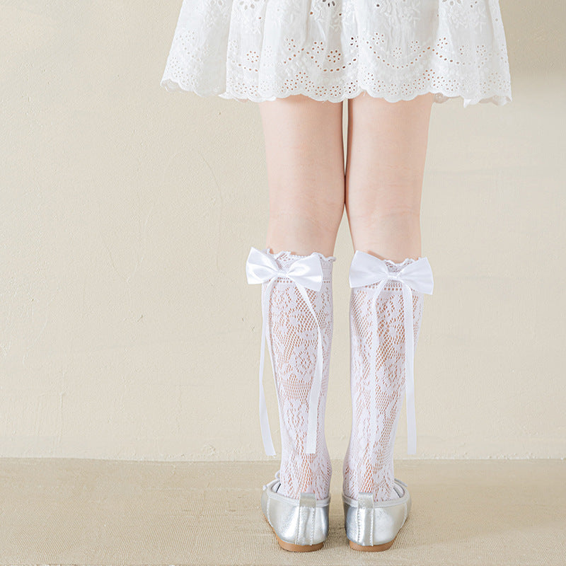 Girls' white floral lace socks with satin bows and long ribbon tails, rear view with silver flats