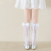 Girls' white floral lace socks with satin bows and long ribbon tails, rear view with silver flats