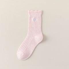 Pink ribbed crew sock with a scalloped cuff and heart-bow embroidery on a beige background