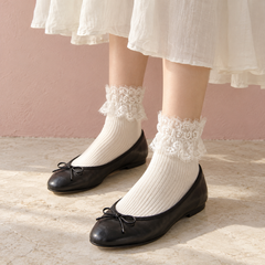 AI standing outfit illustration of White eyelash-lace short socks with an ivory skirt and black ballet flats beside a dusty pink wall.