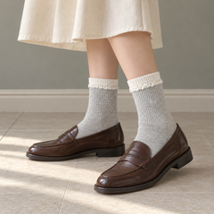 AI standing outfit illustration of Light Gray heart socks with white curled trim, a cream skirt and brown loafers by a sage-gray wall.
