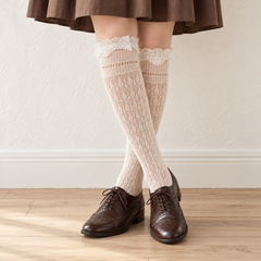 AI styling illustration of Cream diamond-and-leaf trellis long socks with lace cuffs, worn with brown oxford shoes before a warm white wall.