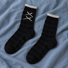 AI flat product illustration of a Black striped-knit sock pair with narrow tulle cuffs and two off-white bows on the observed face, on slate-blue cloth.
