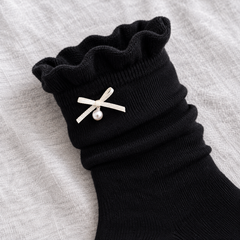 AI product illustration showing the rippled Black sock opening, narrow off-white ribbon bow and single pearl-style drop on gray cotton.