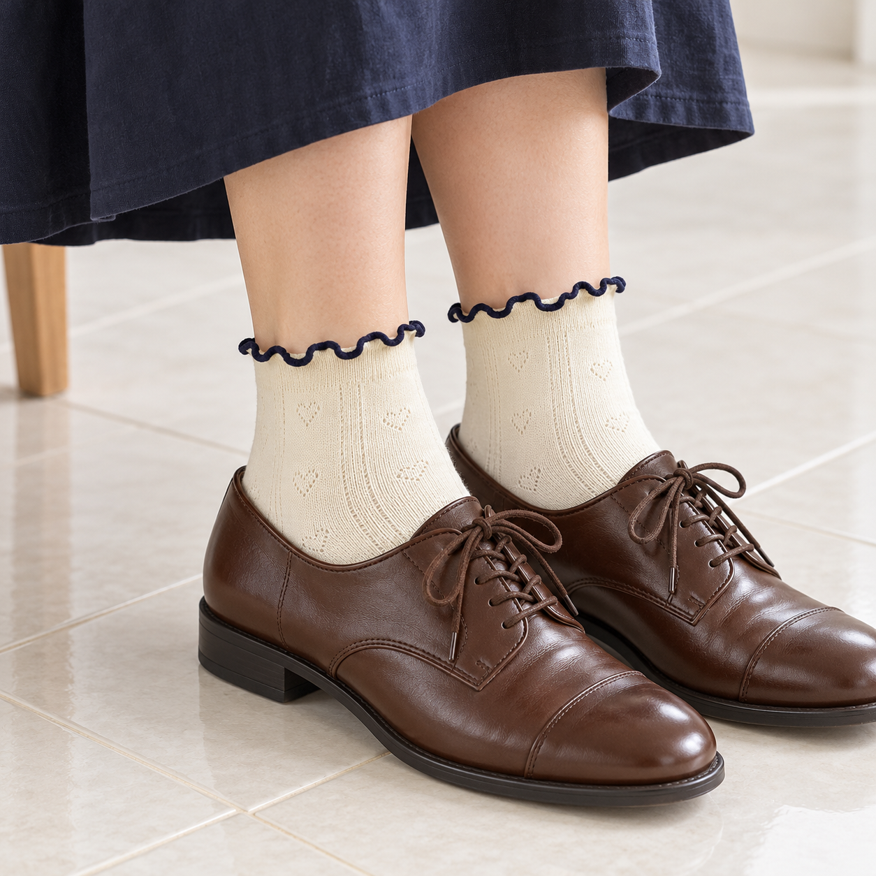 AI styling illustration of Cream heart-pointelle socks with navy wavy edges, brown oxfords and a navy skirt on pale tiles.