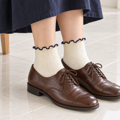 AI styling illustration of Cream heart-pointelle socks with navy wavy edges, brown oxfords and a navy skirt on pale tiles.