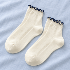 AI flat-lay illustration of a Cream sock pair with sparse heart pointelle and narrow navy wavy openings.