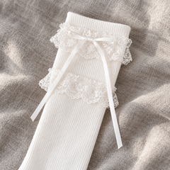 AI detail illustration of the White long sock's two separated floral lace bands, plain knit top and narrow ribbon tails on gray linen.