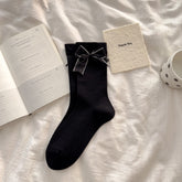 Black crew socks with straight cuffs and broad light-edged bows with small dot accents