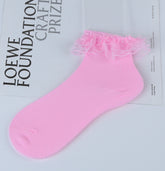 Pink knitted ankle sock with layered pink lace around the cuff, shown on a magazine prop