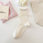 Cream Clover pattern pointelle crew sock with a rolled cuff, small round button and long ribbon bow.