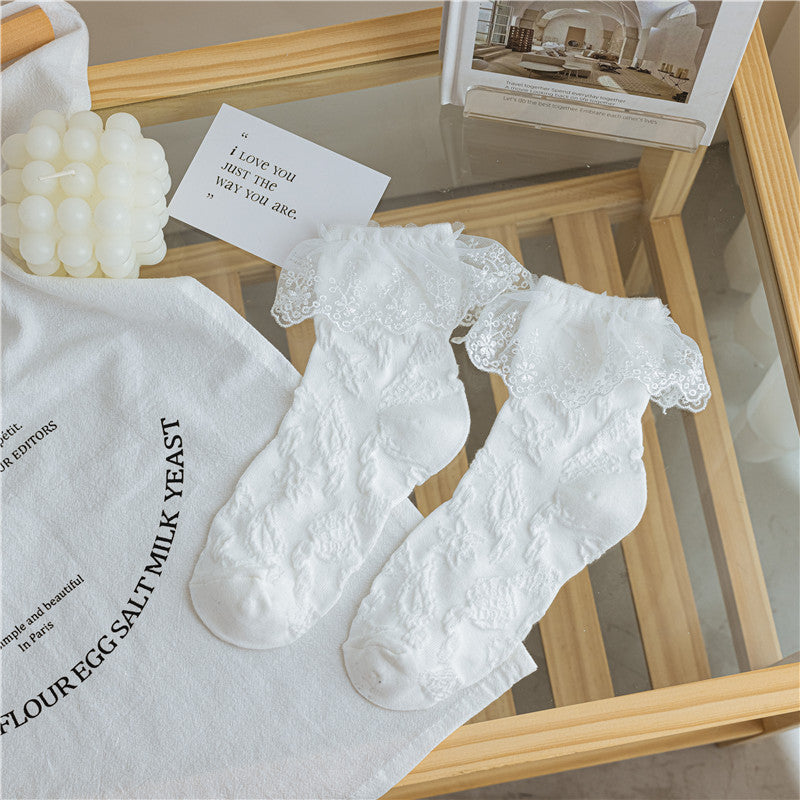 White socks with raised star motifs and wide white floral lace cuffs, laid flat