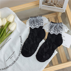 Black socks with raised star motifs and contrasting white floral lace cuffs, laid flat