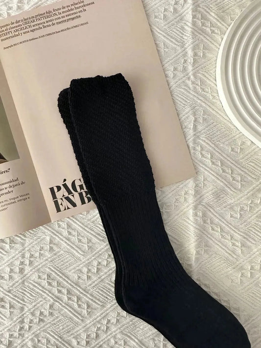A plain black sock laid flat on a magazine over a cream knitted blanket