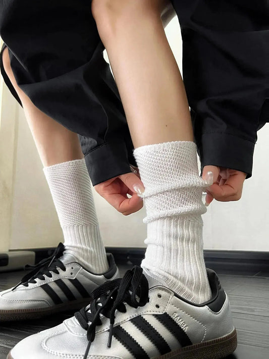 White socks with loose cuffs being folded above grey sneakers with black stripes