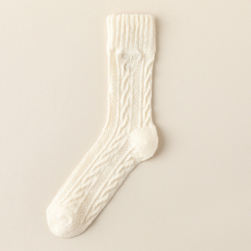 Cream crew sock with twisted cable knit columns, a straight ribbed cuff and a small tonal embroidered bow