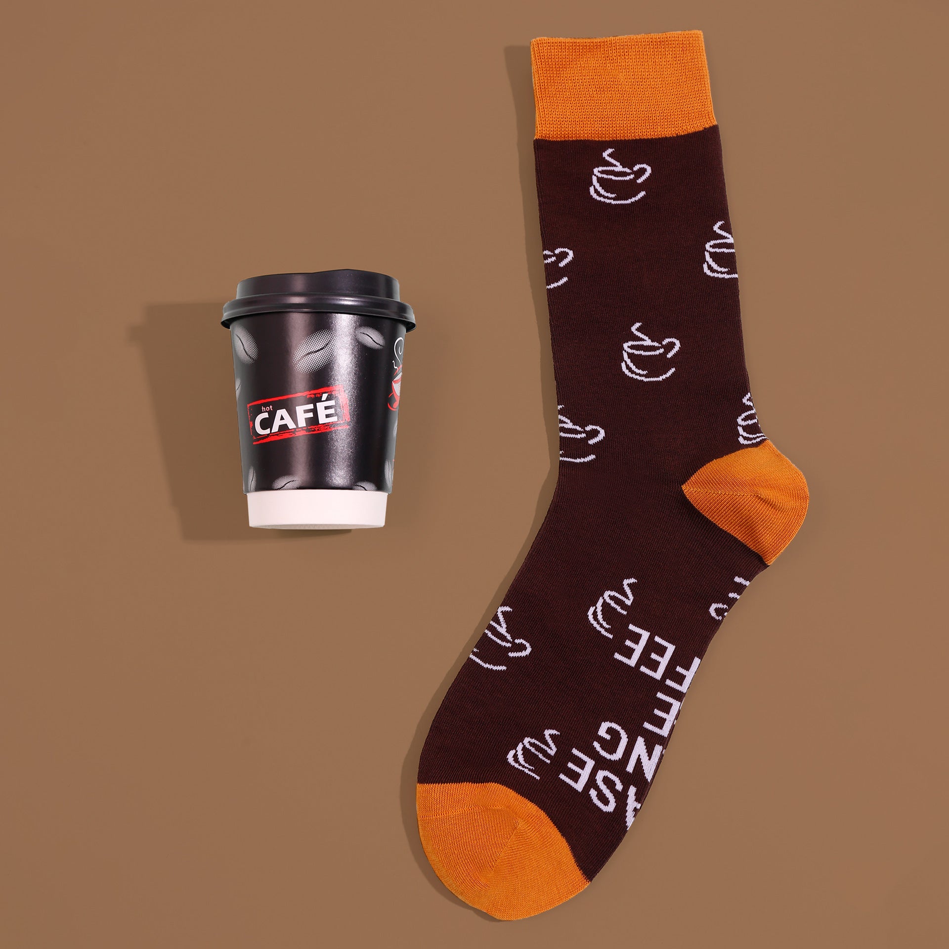 Brown coffee-cup crew sock with orange cuff, heel and toe, beside cup-shaped sock packaging