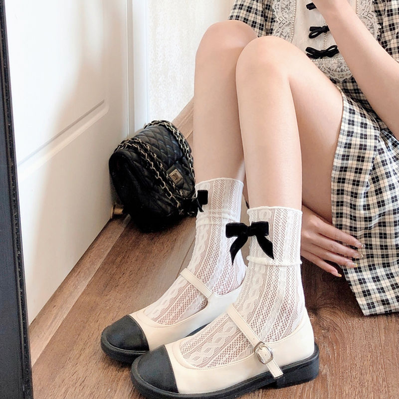 White pointelle socks with broad folded cuffs and large black bows, worn with Mary Janes