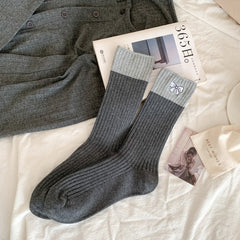 Dark gray ribbed crew socks with broad light gray cuffs and a small embroidered bow, laid flat