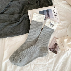Light gray ribbed crew socks with broad cream cuffs and a small outlined embroidered bow, laid flat