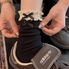 Black ribbed crew sock with a cream crochet-look ruffle cuff and two black bows, worn with separate styling shoes