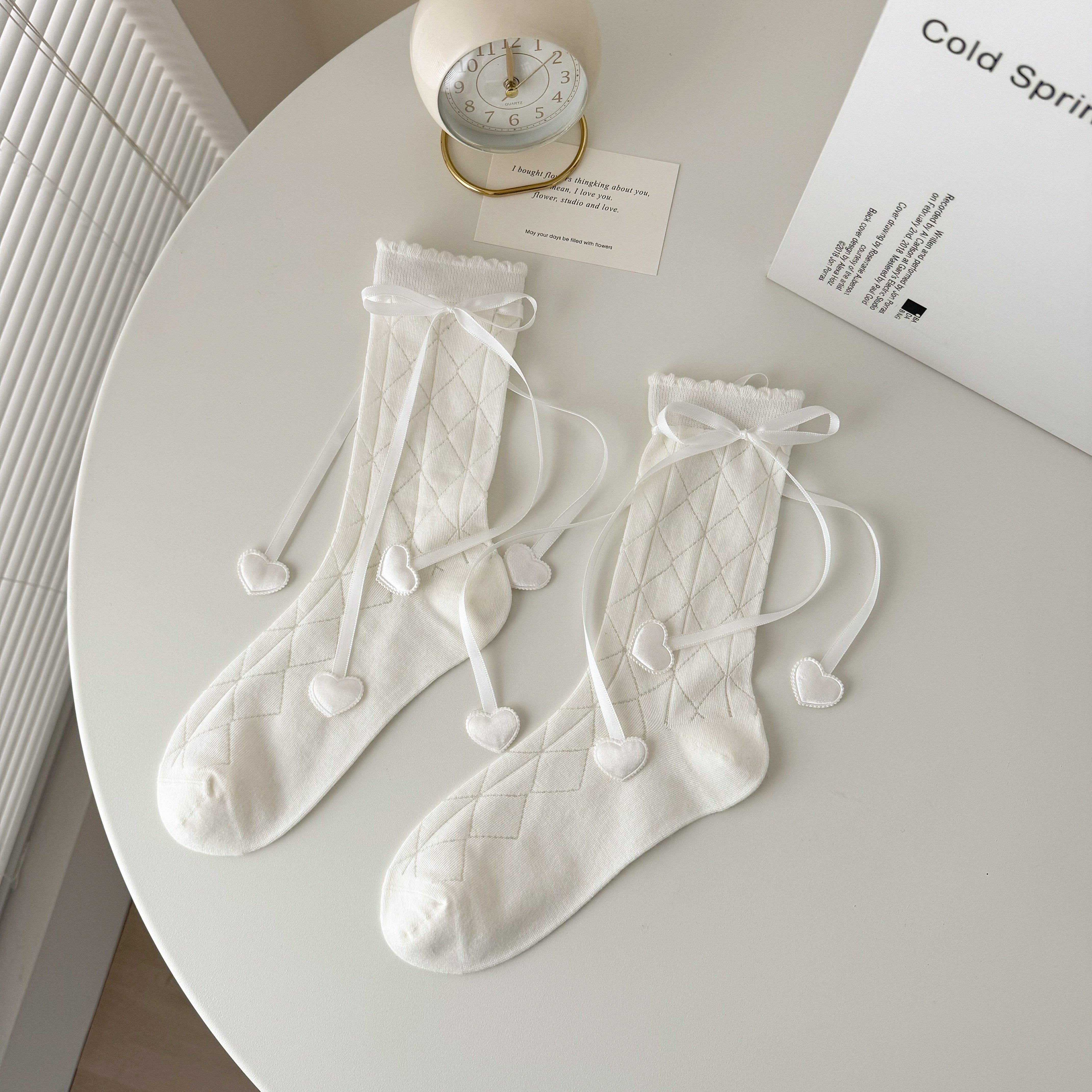 White diamond knit crew socks with scalloped tops, ribbon bows and long tails ending in padded heart shapes.