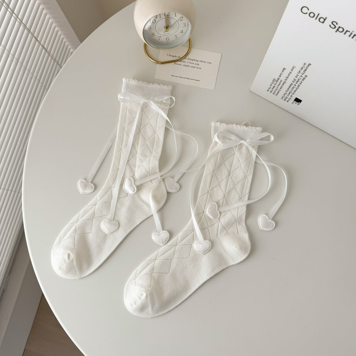 White diamond knit crew socks with scalloped tops, ribbon bows and long tails ending in padded heart shapes.