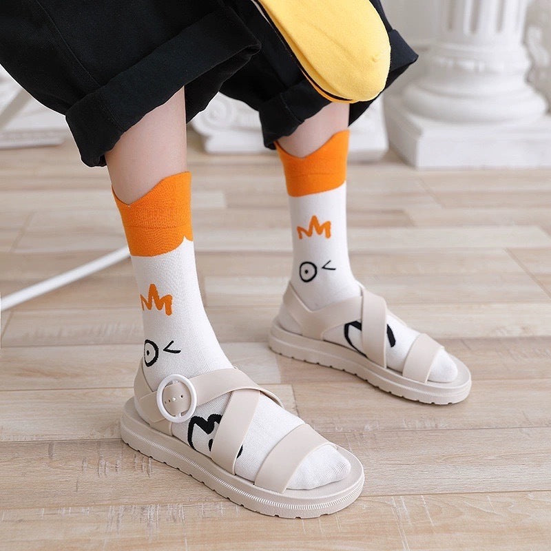 Winking-goose crew socks with orange cuffs worn with cream sandals and cropped black trousers