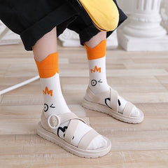 Winking-goose crew socks with orange cuffs worn with cream sandals and cropped black trousers