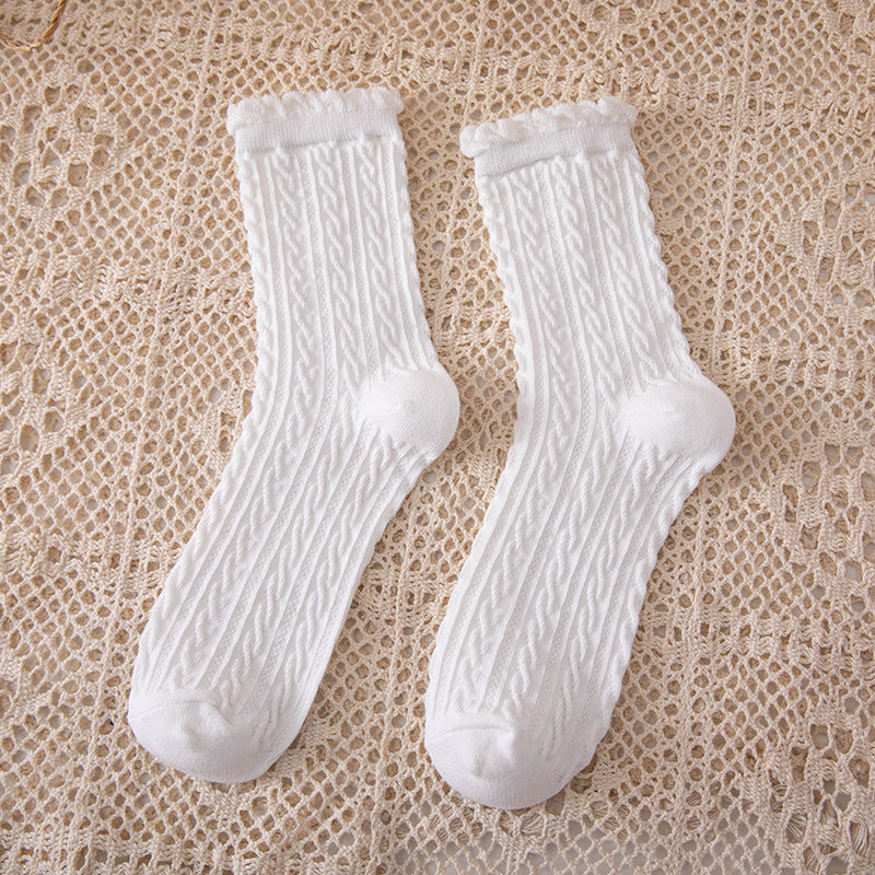 White crew socks with narrow rope-like cable columns and curled cuffs laid on a beige openwork cloth