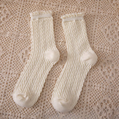 Milk White crew socks with narrow rope-like cable columns and curled cuffs laid on a beige openwork cloth