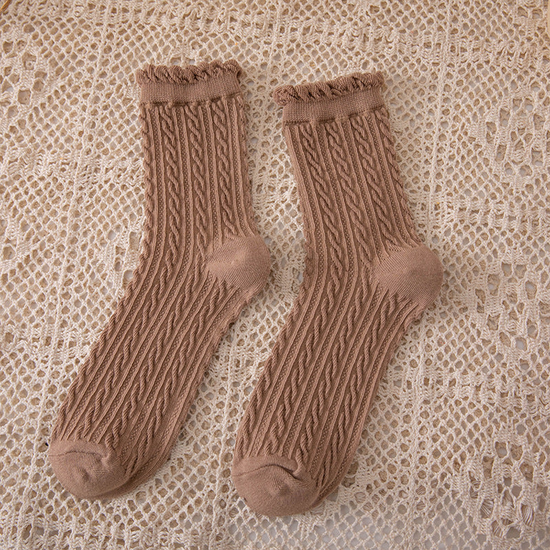 Khaki crew socks in a muted brown shade with narrow cable columns and curled cuffs on a beige openwork cloth