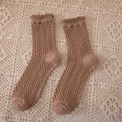Khaki crew socks in a muted brown shade with narrow cable columns and curled cuffs on a beige openwork cloth