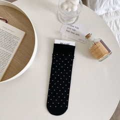 Black polka dot sock with white dots and a broad ribbed cuff, laid flat