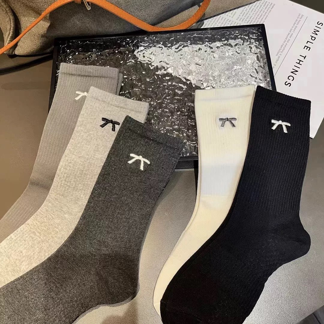 Five fine ribbed mini bow sock colors laid flat, from left Gray, Light Gray, Dark Gray, Cream and Black; colors sold separately by the pair