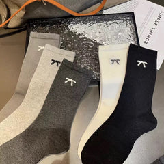 Five fine ribbed mini bow sock colors laid flat, from left Gray, Light Gray, Dark Gray, Cream and Black; colors sold separately by the pair