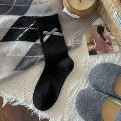 Black ribbed crew sock with a gray gingham bow below its broad cuff, shown flat beside styling props