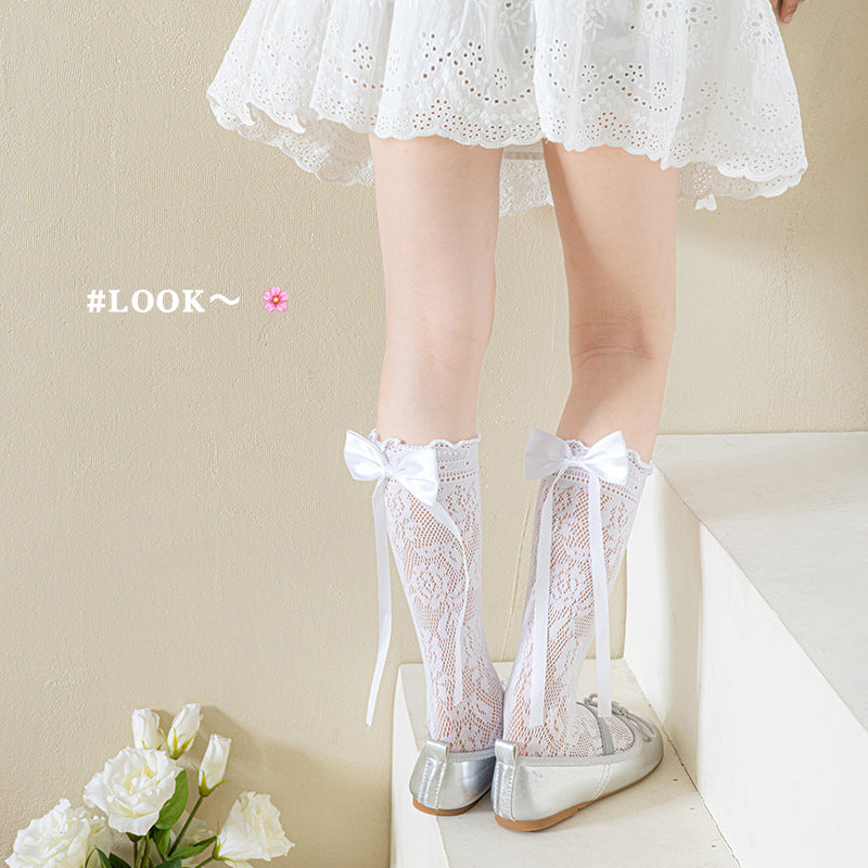 Girls' white floral lace bow socks shown from the side with a white dress and silver flats