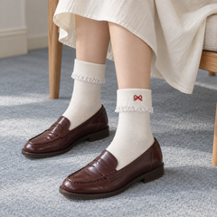 AI styling illustration of White fold-over ribbed socks with tiny red embroidered bow detail, lace edging and dark brown loafers in a high-oblique seated outfit
