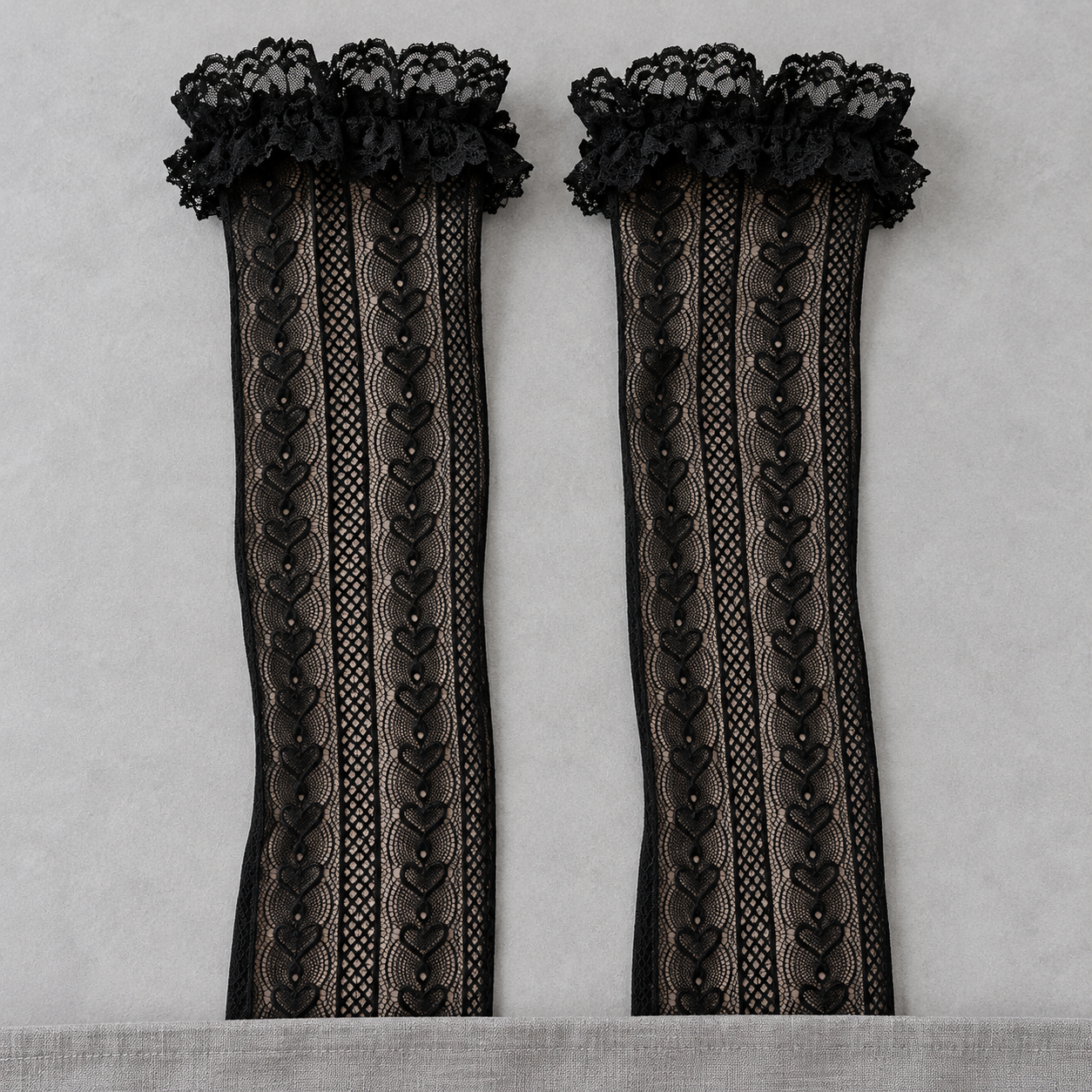 AI product illustration of Black long linked-heart mesh shafts and broad scalloped lace cuffs on a gray surface, with lower ends concealed.