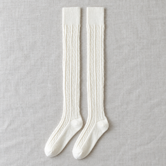 AI product illustration of a Cream long-sock pair on gray linen, showing narrow cable columns, plain straight cuffs and shaped feet.