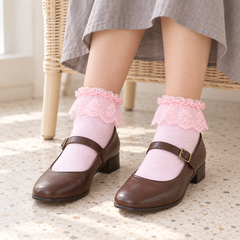 AI seated styling illustration of Pink floral lace-flounce ankle socks with brown Mary Janes and a gray skirt beside a wicker chair.