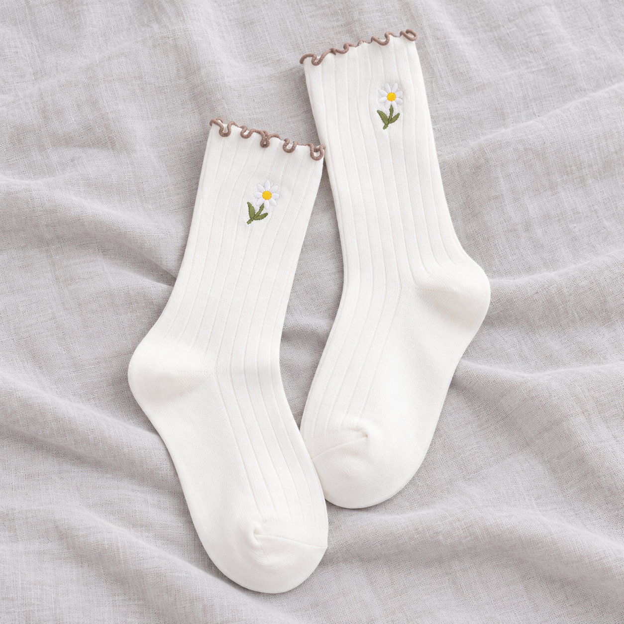 AI product illustration of an empty White matching ribbed pair with stemmed daisy embroidery and narrow brown wavy edges on gray linen.
