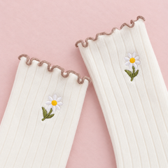 AI close product illustration of White ribbed upper shafts with one small stemmed daisy each and narrow brown wavy edges on muted pink paper.