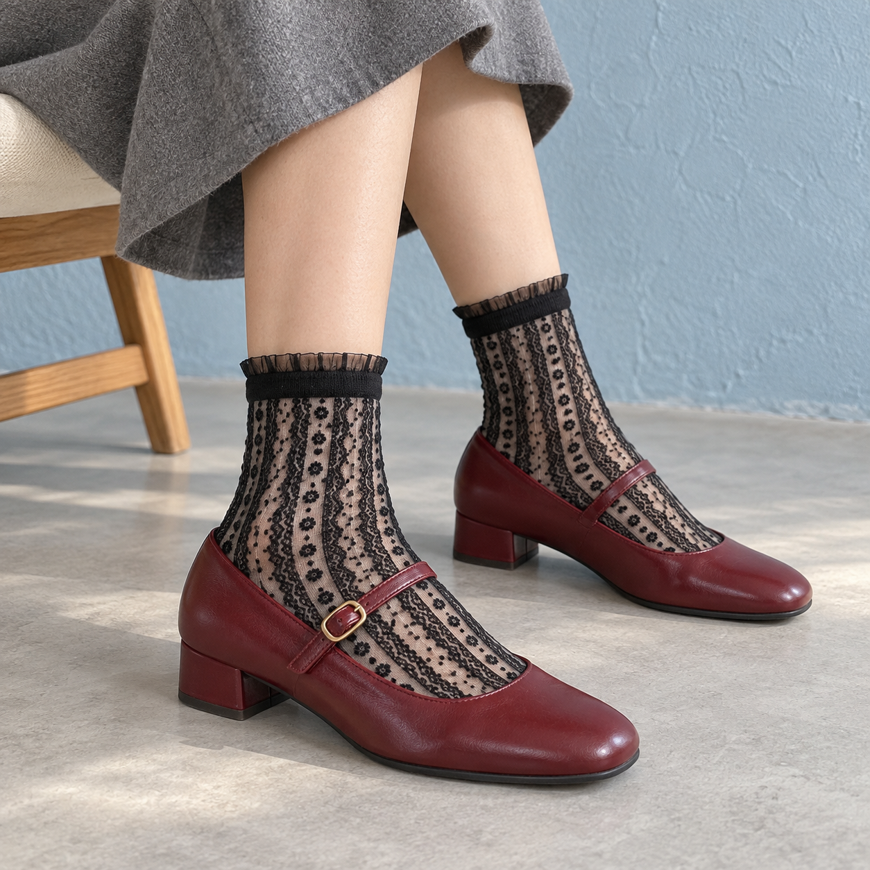 AI styling illustration of Black sheer flower-chain socks with wine-red Mary Janes and a gray skirt, seated by a mist-blue wall.