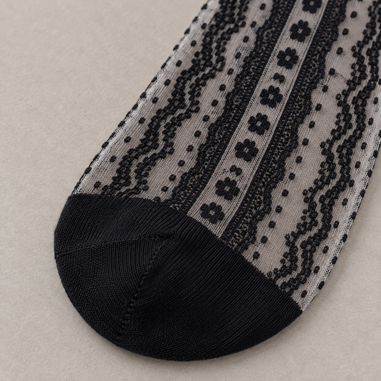 AI product detail illustration of the solid Black toe panel meeting the sheer flower-chain and dotted stripe pattern on the sock front.